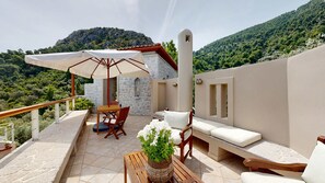 Una terraza con una mesa, sillas, un sofá y una sombrilla, con vistas a un paisaje montañoso.