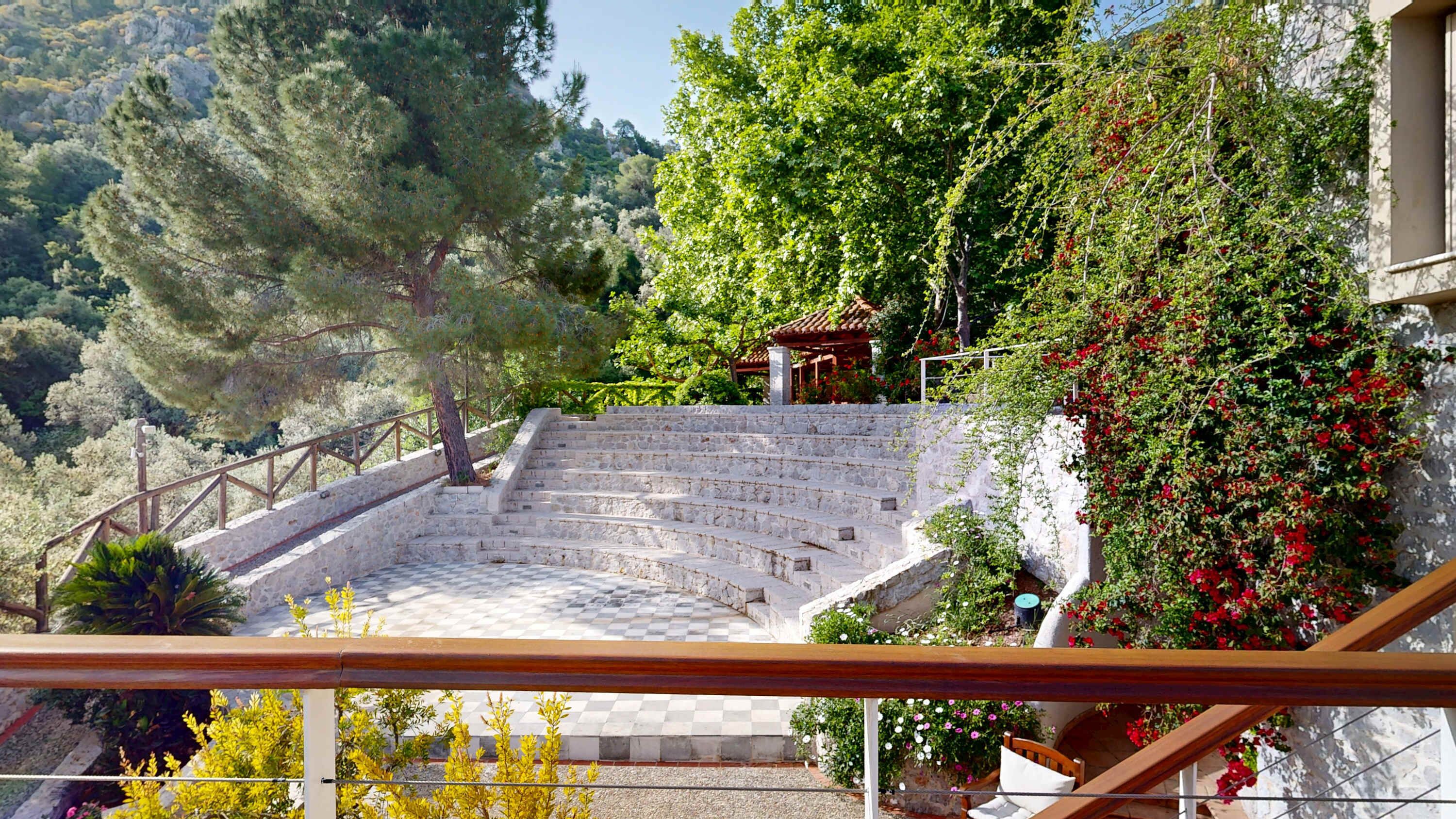 A stone staircase leading to a wooden gazebo surrounded by lush greenery and flowering plants.