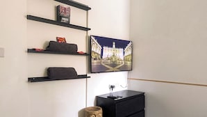 Ett rum med en TV som är monterad på väggen, en svart byrå och hyllor med diverse föremål.