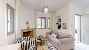 Un salon avec une cheminée, un canapé à rayures, une table basse ronde et un luminaire suspendu.