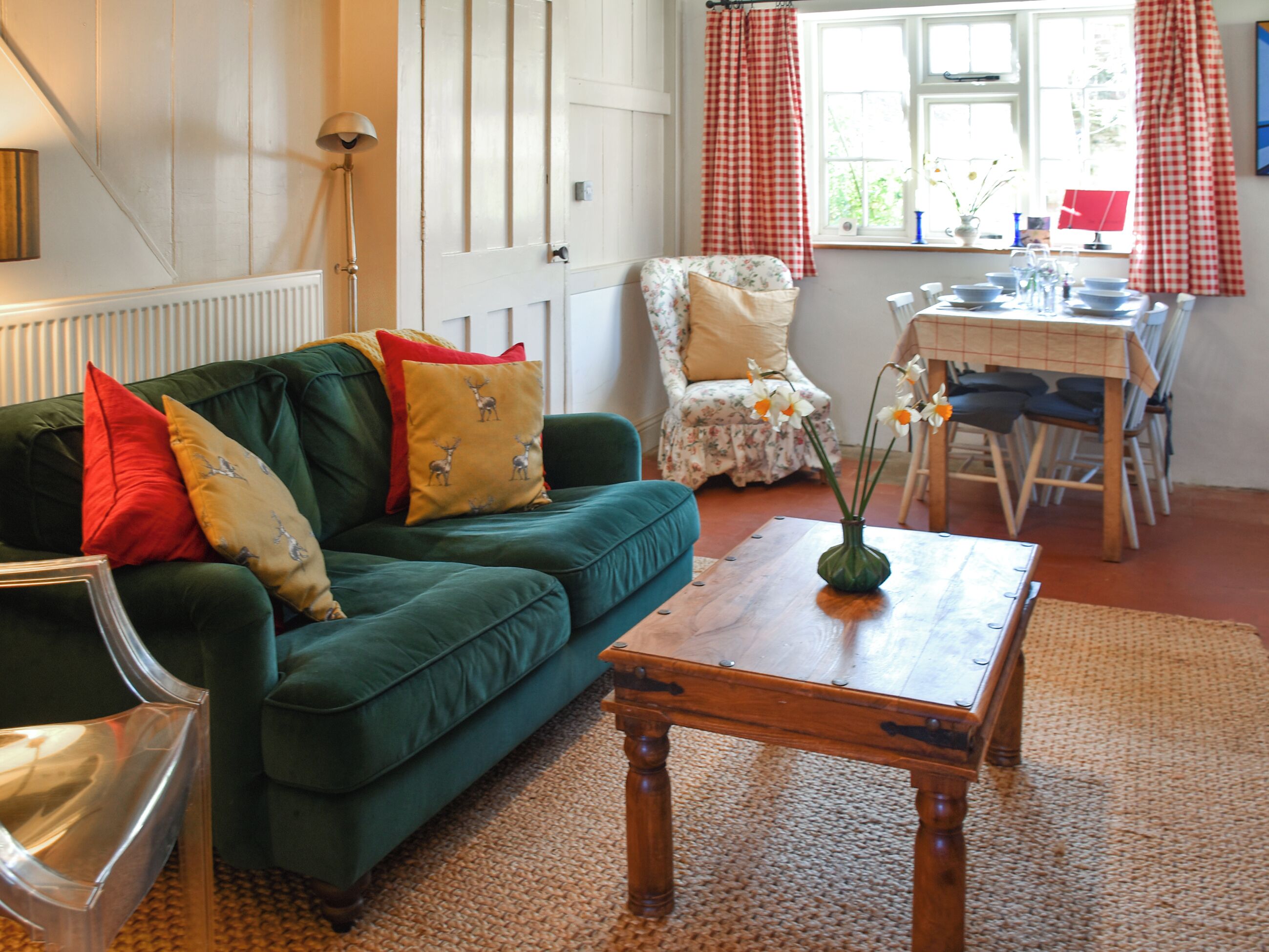Ein Wohnzimmer mit einem grünen Sofa, einem Holztisch, einem blumigen Sessel und einem Esstisch mit Stühlen.