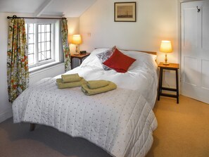 A bedroom with a bed, two bedside lamps, a window with curtains, a door, and a framed picture on the wall.