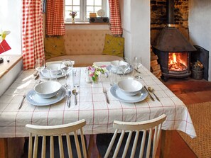 Une table à manger dressée avec des assiettes, des verres et des couverts, un canapé avec des coussins, une fenêtre avec des rideaux et un poêle à bois.