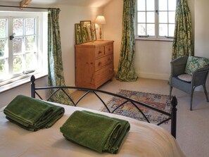 Une chambre à coucher avec un lit, une commode en bois, une chaise et une fenêtre avec des rideaux.