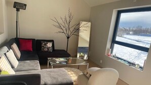 Ein Wohnzimmer mit Sofa, Sessel, Couchtisch und einem großen Fenster mit Blick auf eine verschneite Landschaft.