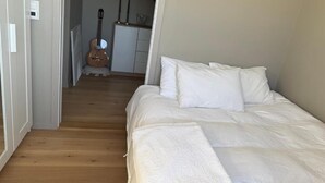 Ein Schlafzimmer mit Bett, weißer Bettwäsche, einer Gitarre und einer Treppe, die in einen Küchenbereich führt.