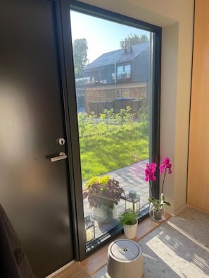 Ein Zimmer mit einer Schiebetür zum Garten, einem kleinen Tisch mit einem Blumentopf und einem dekorativen Gegenstand auf dem Boden.