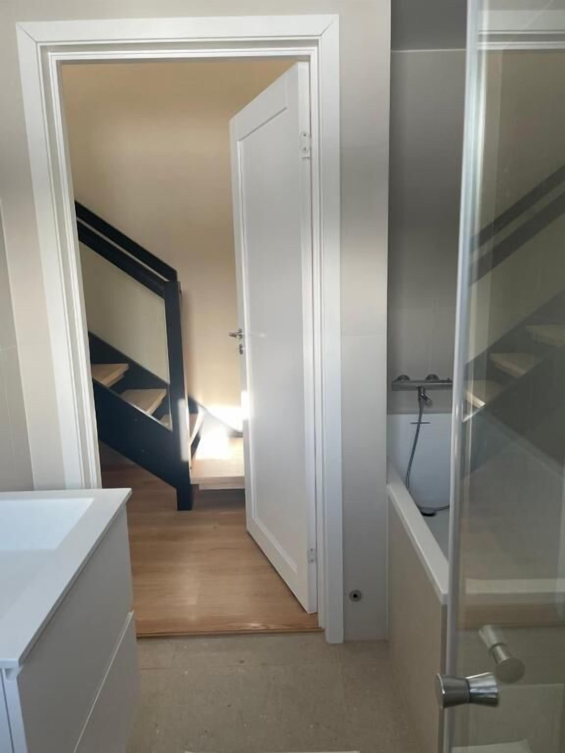 Ein Flur mit Treppe zu einem Zimmer, einer Tür und einem Duschbereich.