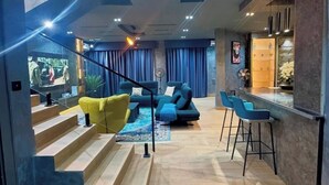 A modern living room with a staircase, a bar area, and a seating area with blue and yellow sofas. - Eseose Apartment (Abuja)