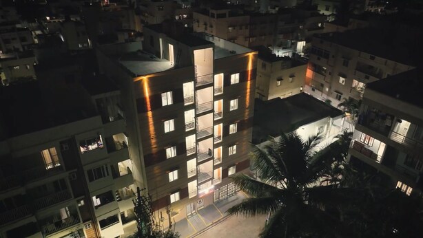 A multi-story building with balconies, a parking area, and a palm tree. - Odilia Apartelle (Bengaluru)