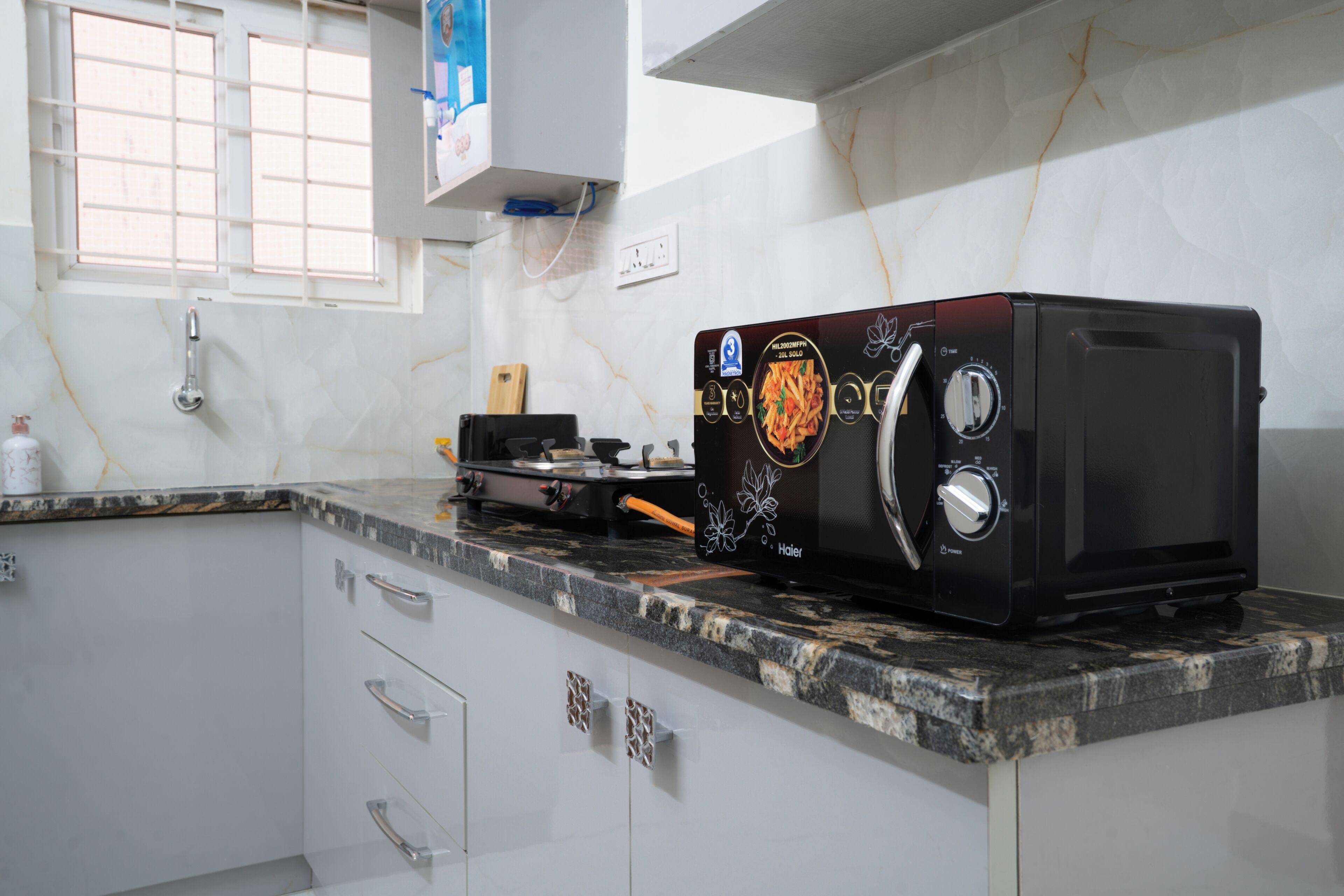 A kitchen with a black toaster oven on the counter, a window with blinds, and a white cabinet with drawers.