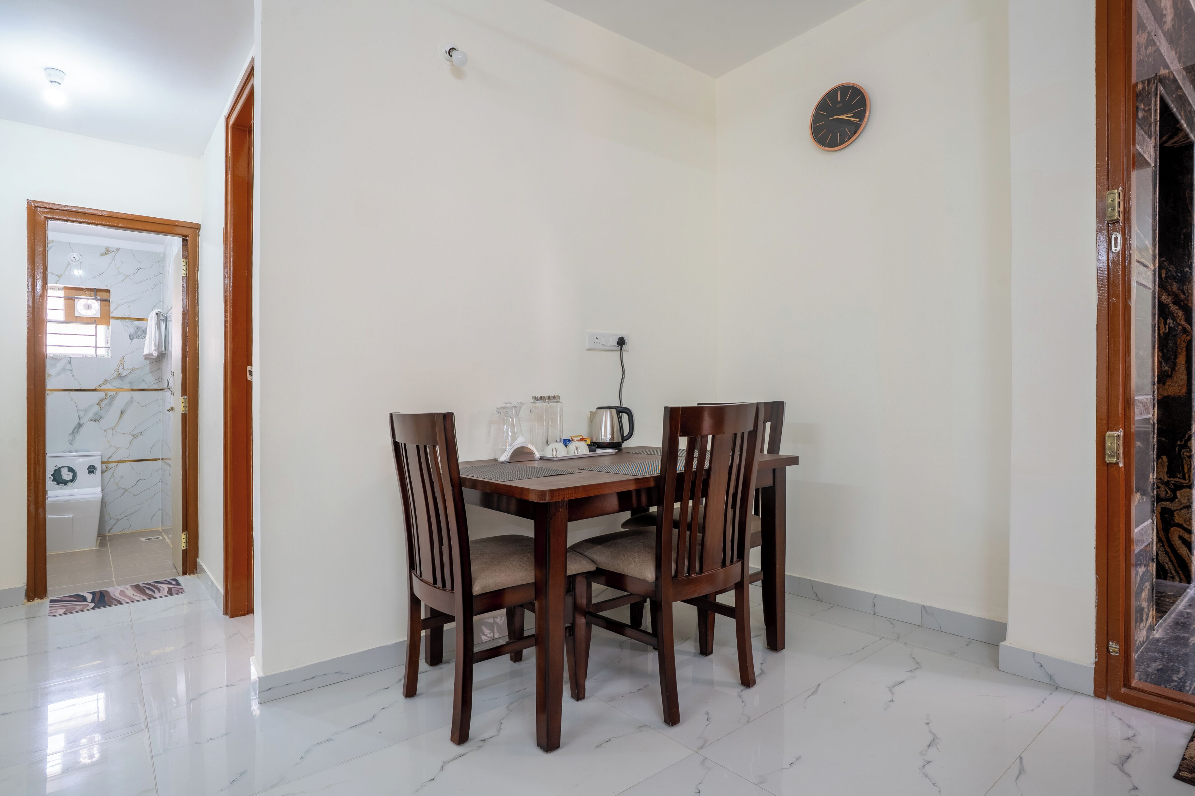 A dining area with a wooden table and four chairs, a clock on the wall, and a tiled floor.