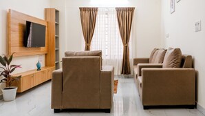 A living room with a flat-screen TV, two sofas, a coffee table, a potted plant, and a ceiling light fixture. - Odilia Apartelle (Bengaluru)