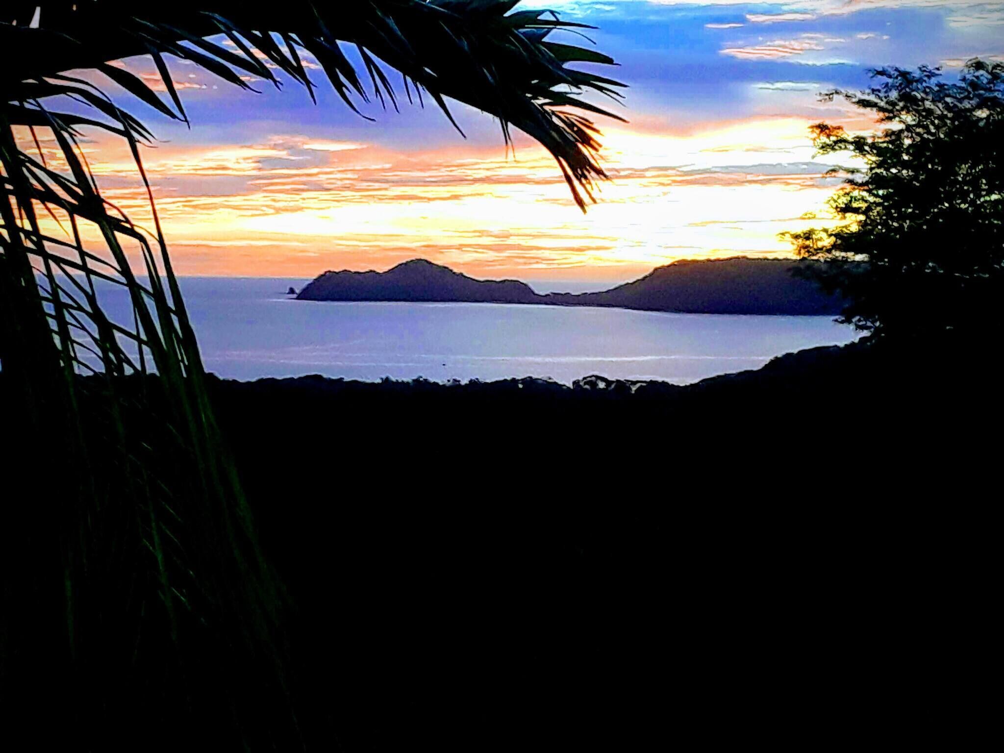 Eine Küstenlandschaft mit Sonnenuntergang, Palmen und fernen Inseln.