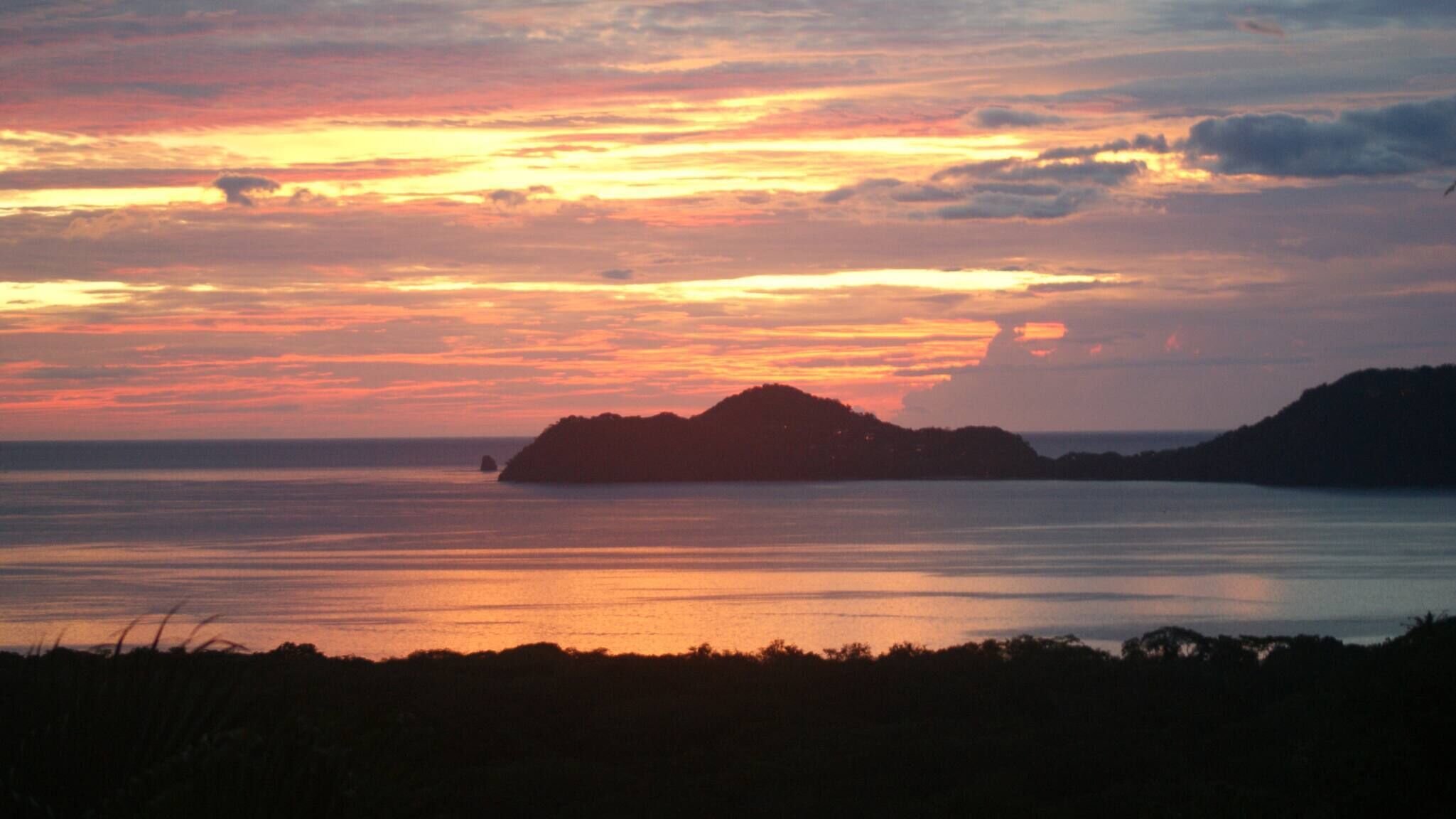 A sunset over a calm sea with a silhouette of an island.