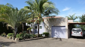 A house with a garage, palm trees, and a stone wall. - Tranquil Poolside Retreat in Playa Panama, Papagayo Bay (Playa Panama,Papagayo Bay)
