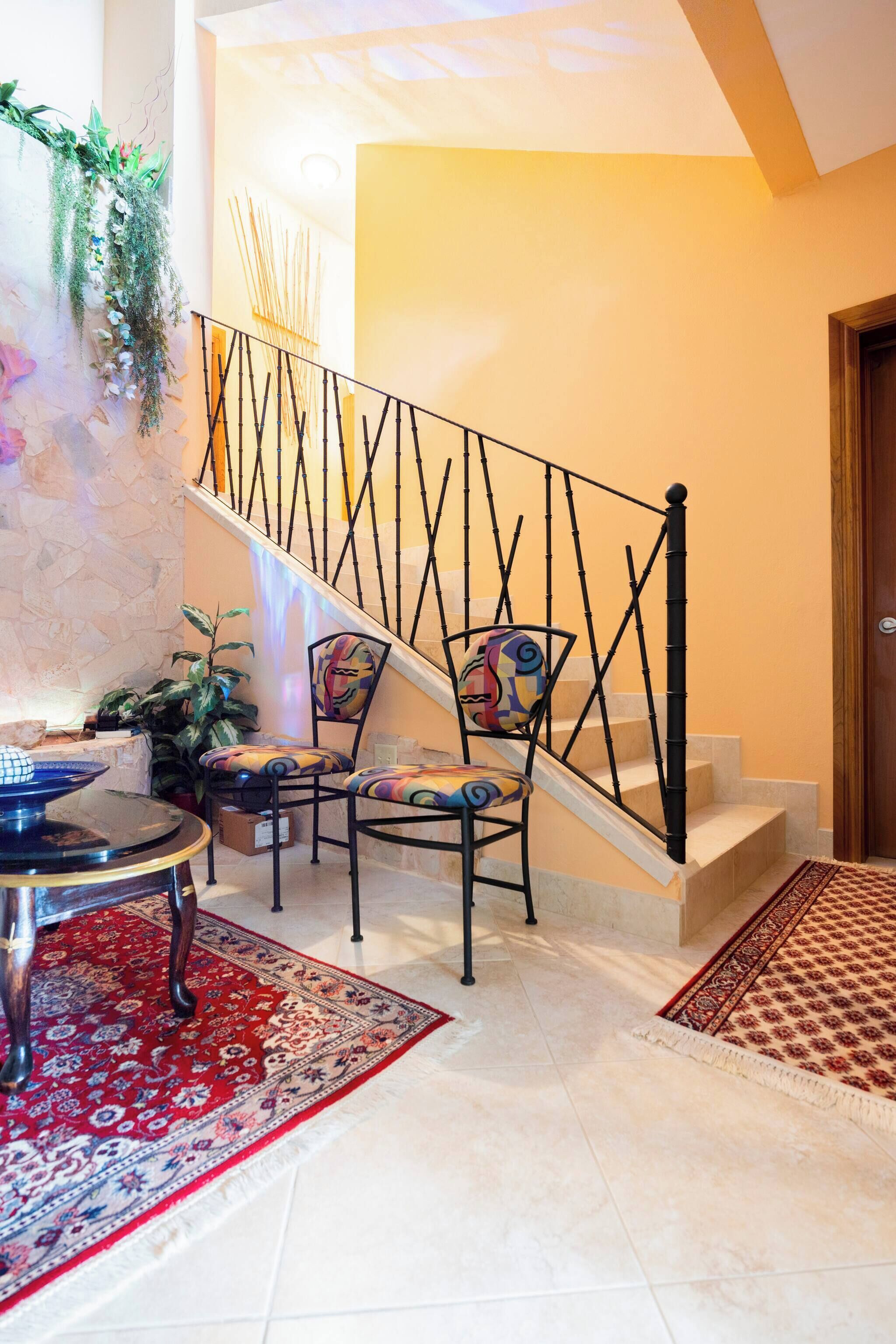 A staircase with a geometric railing, a patterned rug, and a chair with a colorful design.