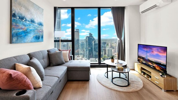 Un soggiorno moderno con un divano grigio, un tavolino rotondo, una televisione a schermo piatto e un'ampia finestra con vista sulla città.