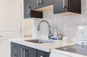 A kitchen with a double sink, dark cabinets, white countertop, and a built-in stove.