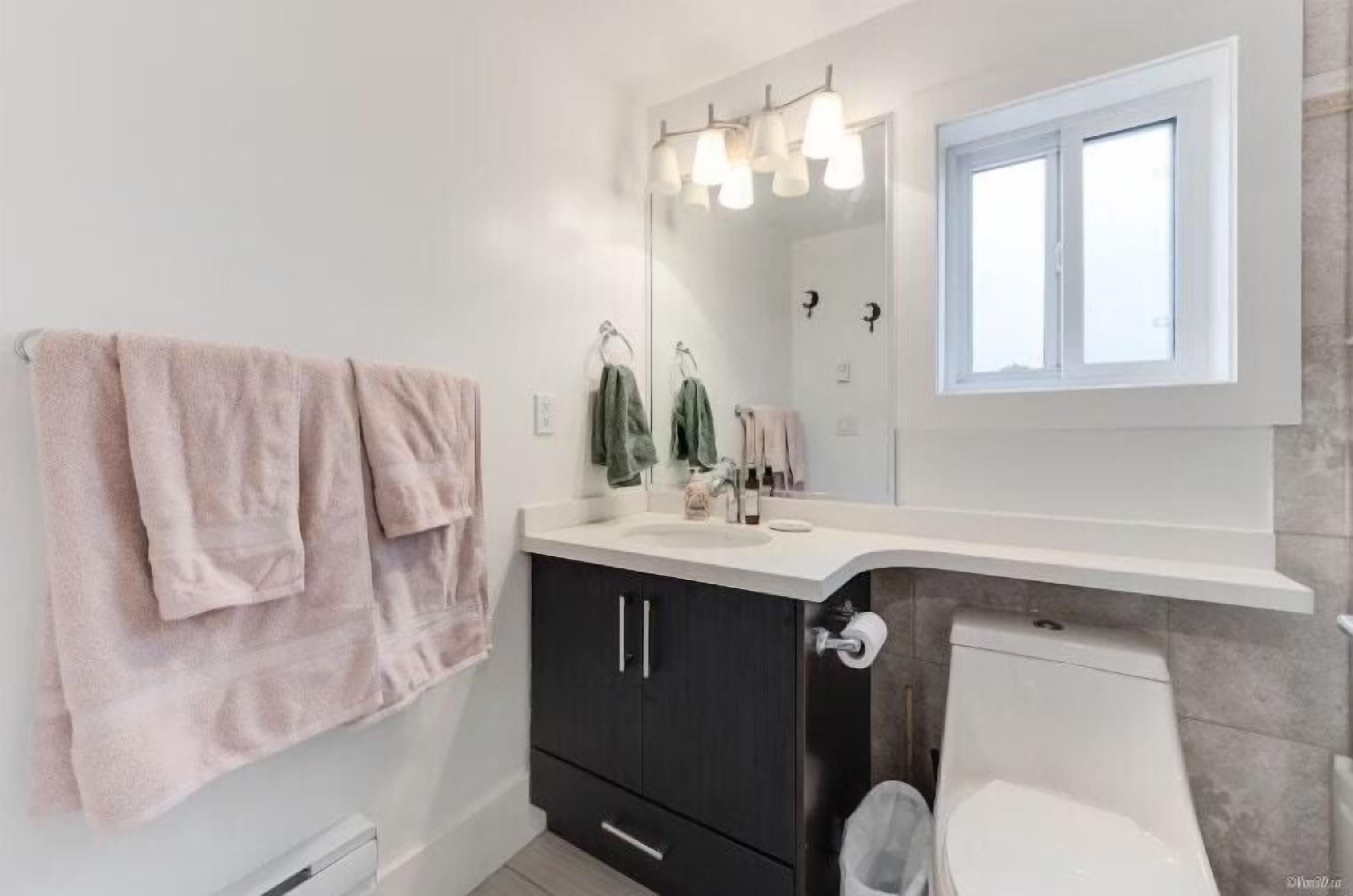 Un baño con lavamanos blanco, muebles oscuros, un espejo y una ventana.