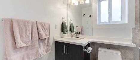 Un baño con lavamanos blanco, muebles oscuros, un espejo y una ventana.