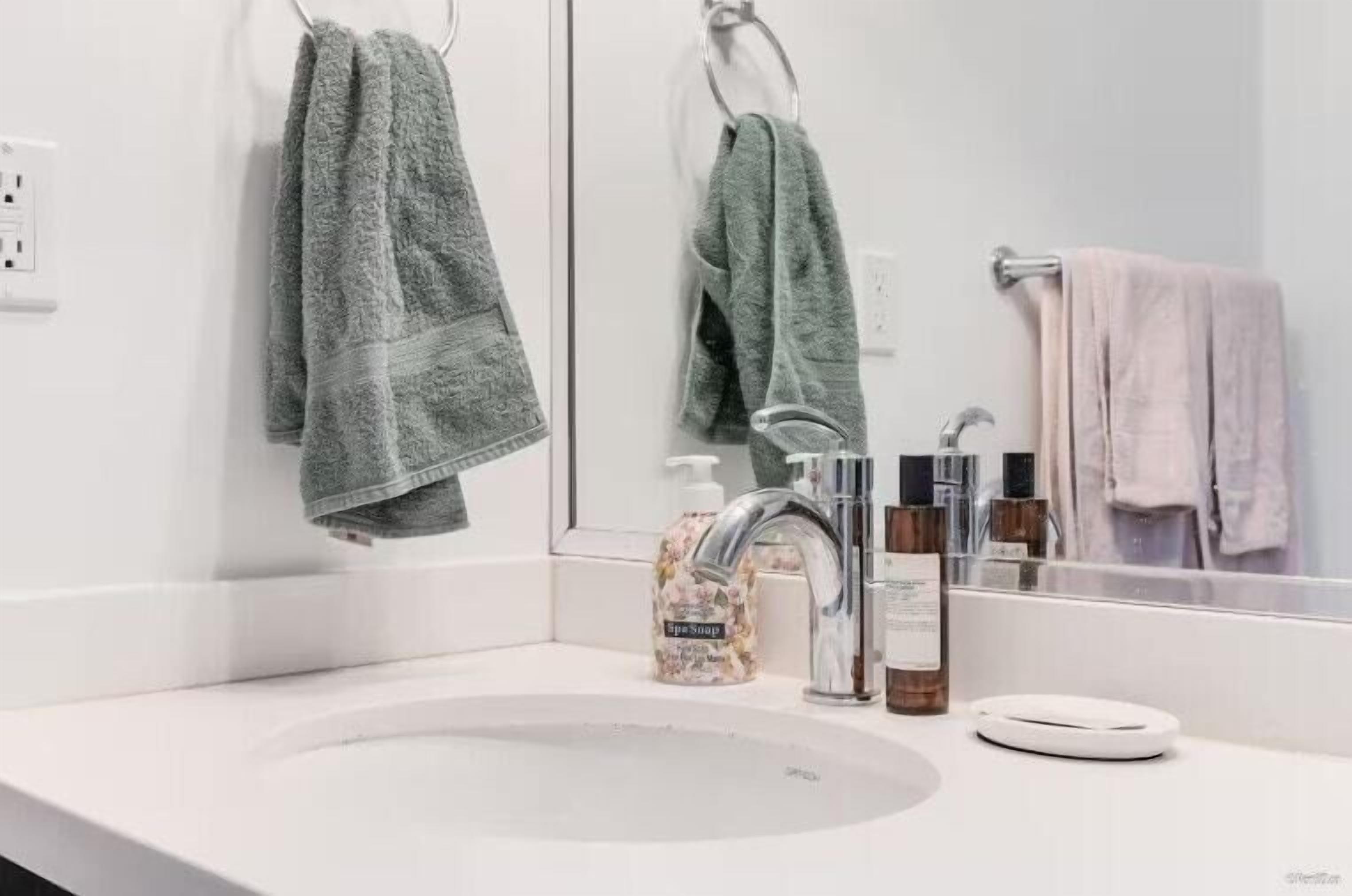 A bathroom with a white sink, a mirror, a towel rack with a green towel, and a soap dispenser.