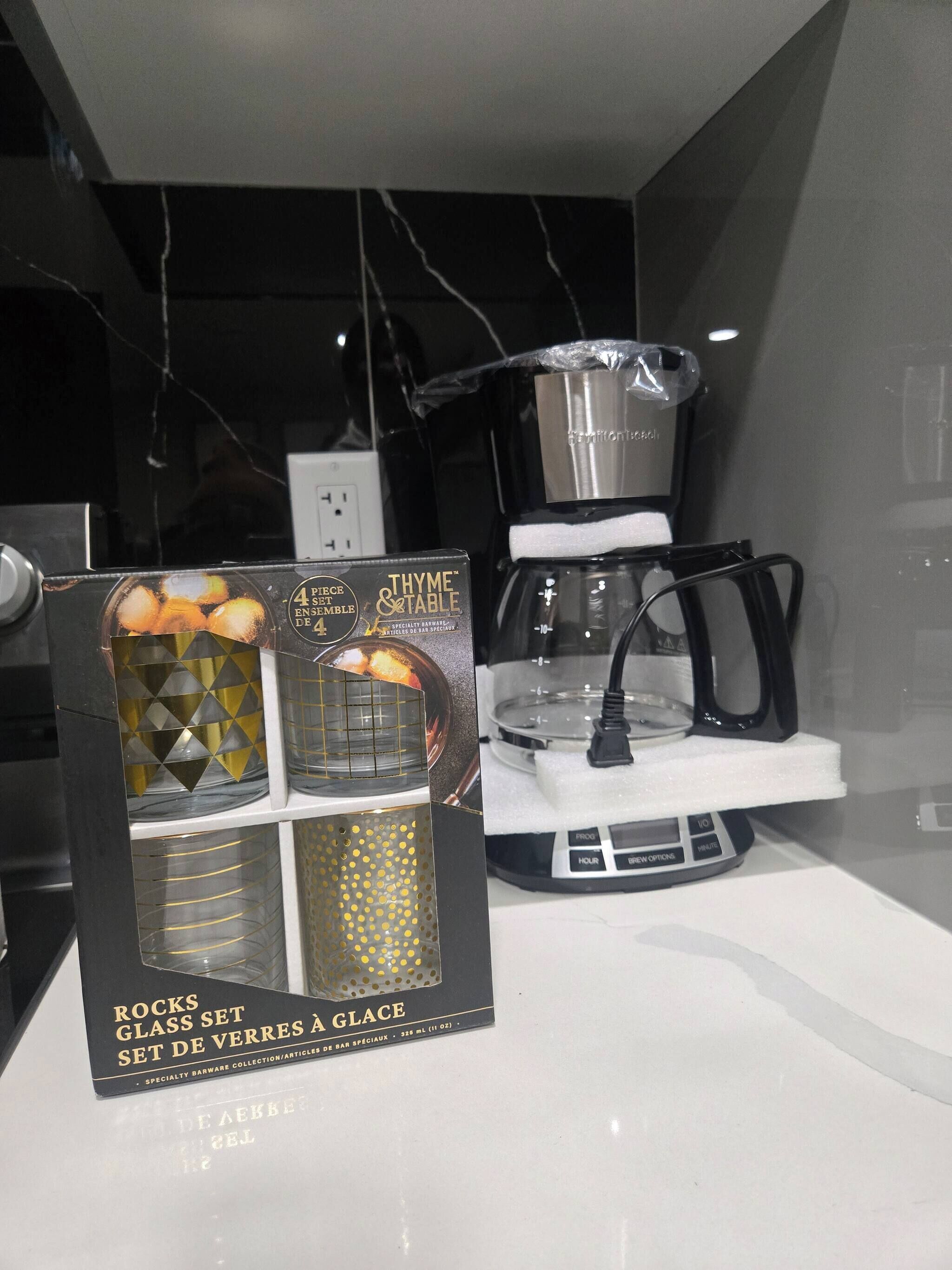 A kitchen area with a coffee maker, a glass set, and a box of Thyme & Table specialty barware.