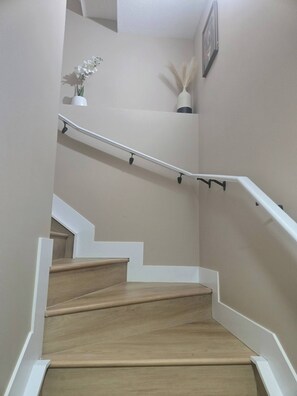 A staircase with wooden steps and white handrails, leading to a landing with a vase of white flowers. - "Your Home Away From Home" (Edmonton)