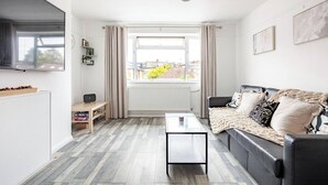 Ein modernes Wohnzimmer mit einer Couch, einem Couchtisch, einem Fernseher und einem Fenster mit Vorhängen.