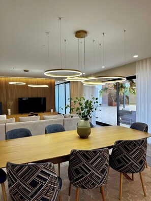 A modern dining area with a long table, patterned chairs, a vase with plants, and a TV in the background. - Sandoco House - Pitch&Putt Golf - Pool & Nature (Arcozelo)