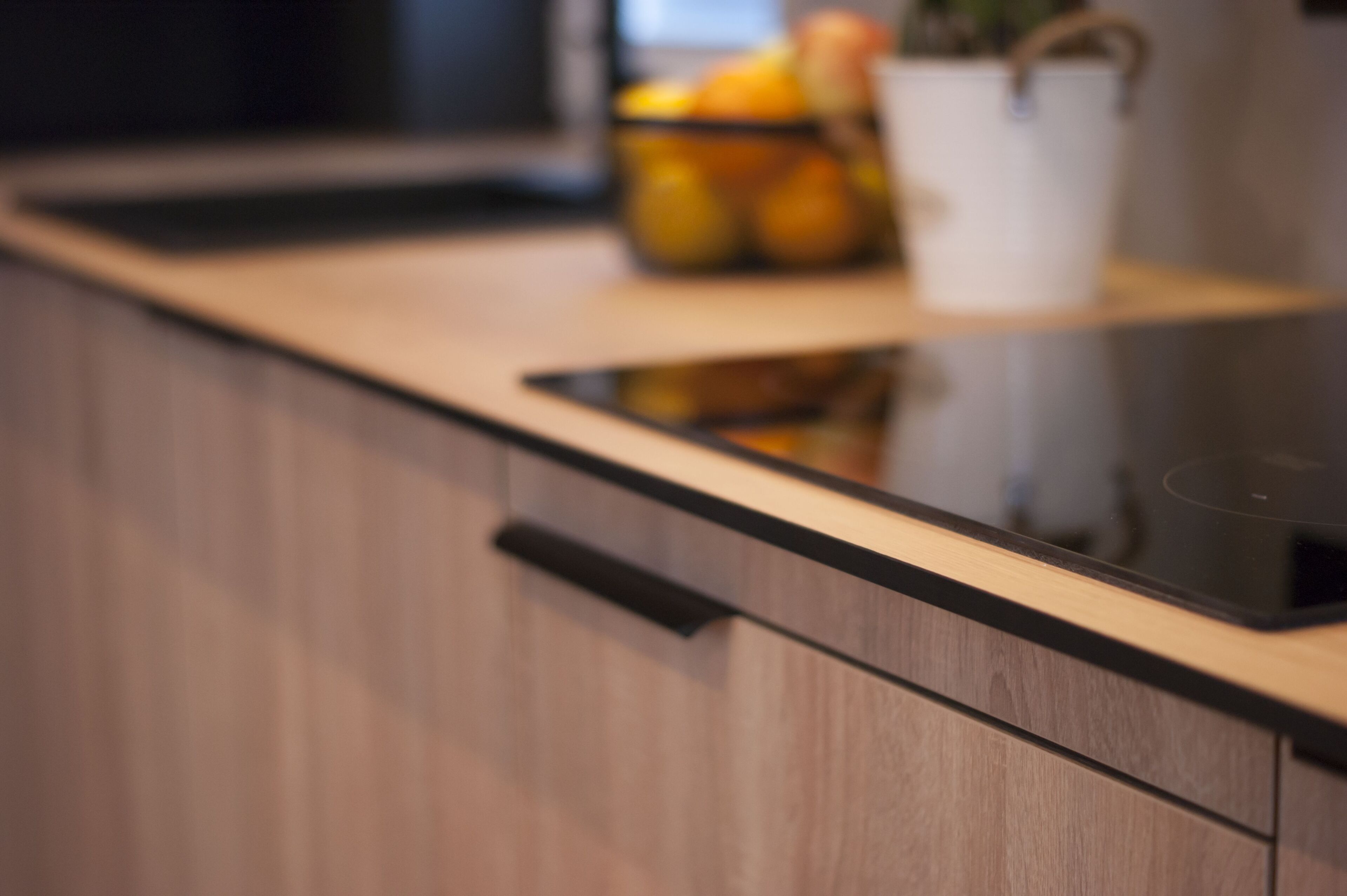 A kitchen with a wooden countertop, a black induction cooktop, and a white container with fruits.