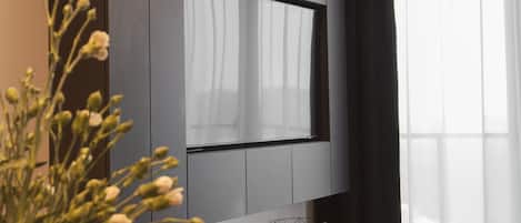 Una sala moderna con un televisor de pantalla plana montado en una pared oscura, una mesa de comedor con un jarrón de flores y un sofá.