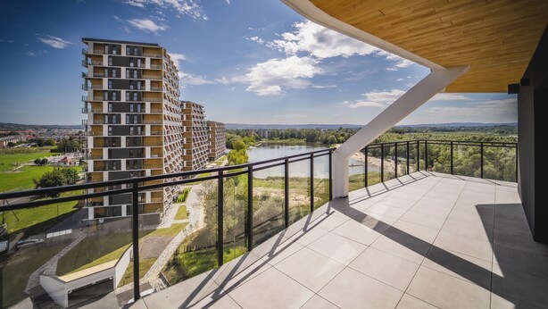 Een modern gebouw met een balkon met uitzicht op een rivier en groen.