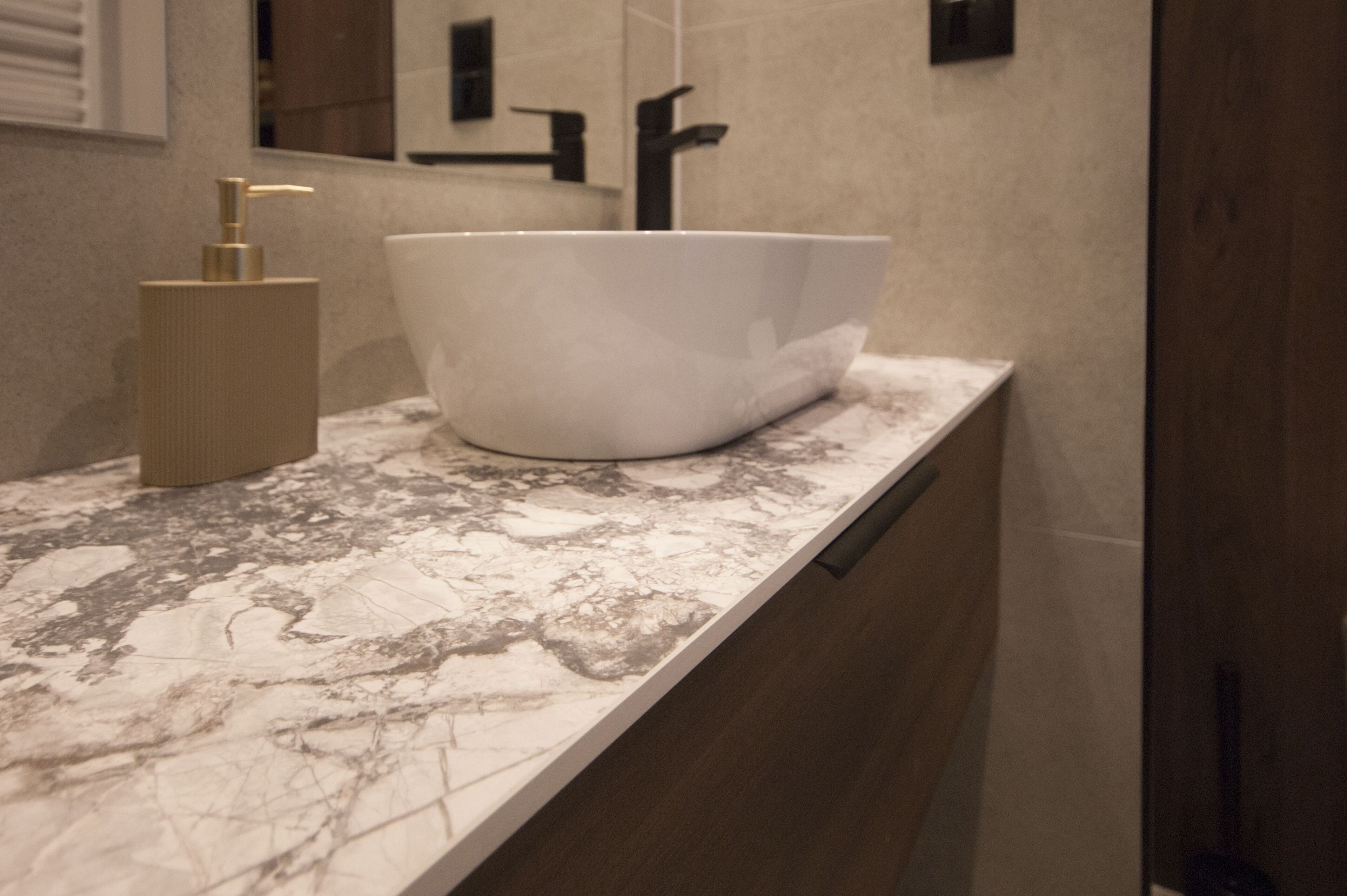 A bathroom with a white vessel sink, a gold pump, and a marble countertop.