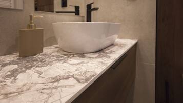 A bathroom with a white vessel sink, a gold pump, and a marble countertop.
