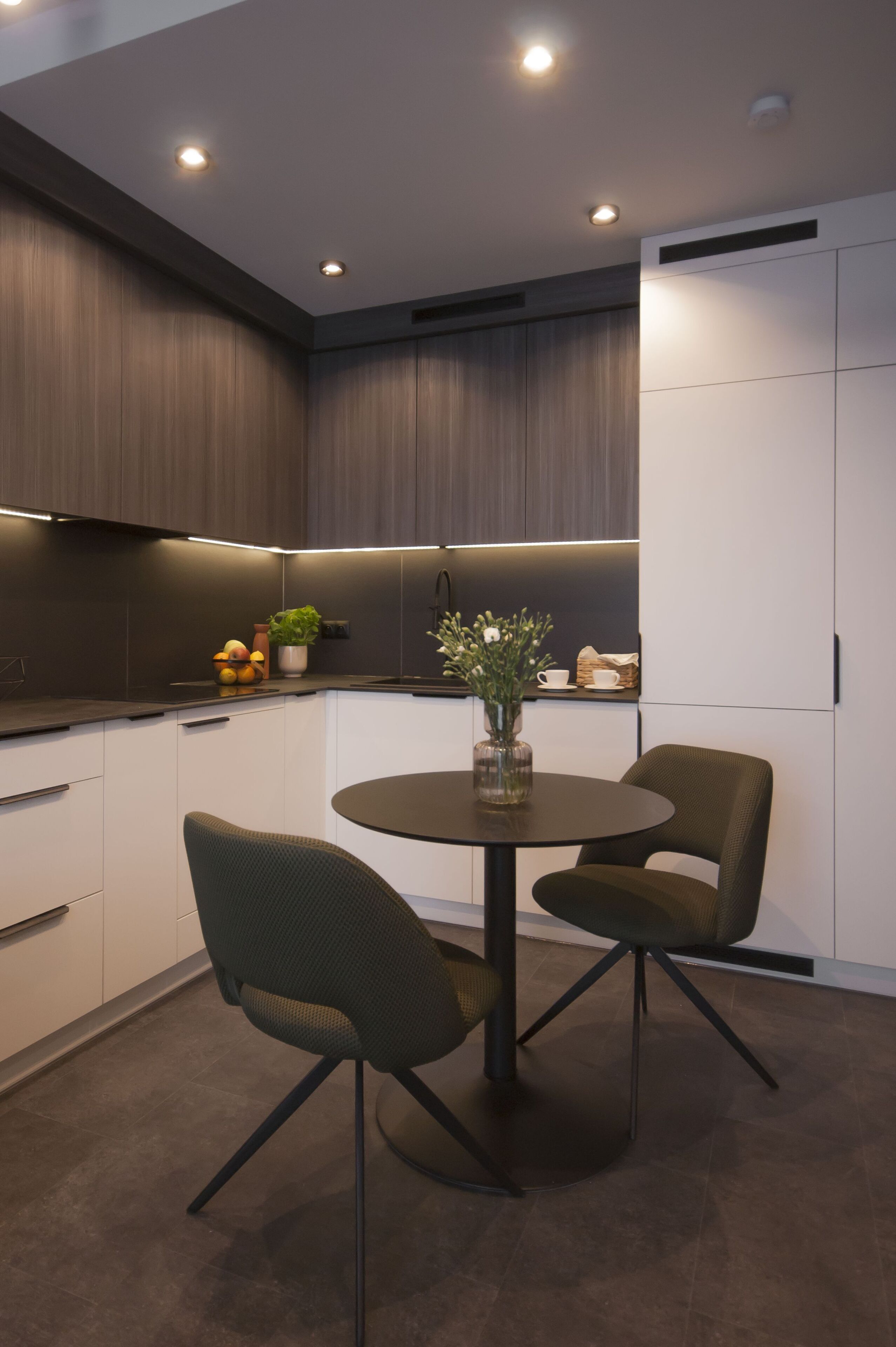 A modern kitchen with dark wood cabinets, a round table with two chairs, and a vase with flowers.