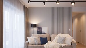 Een moderne woonkamer met een bank, een bijzettafeltje met een boek en fruit, en een lamp.