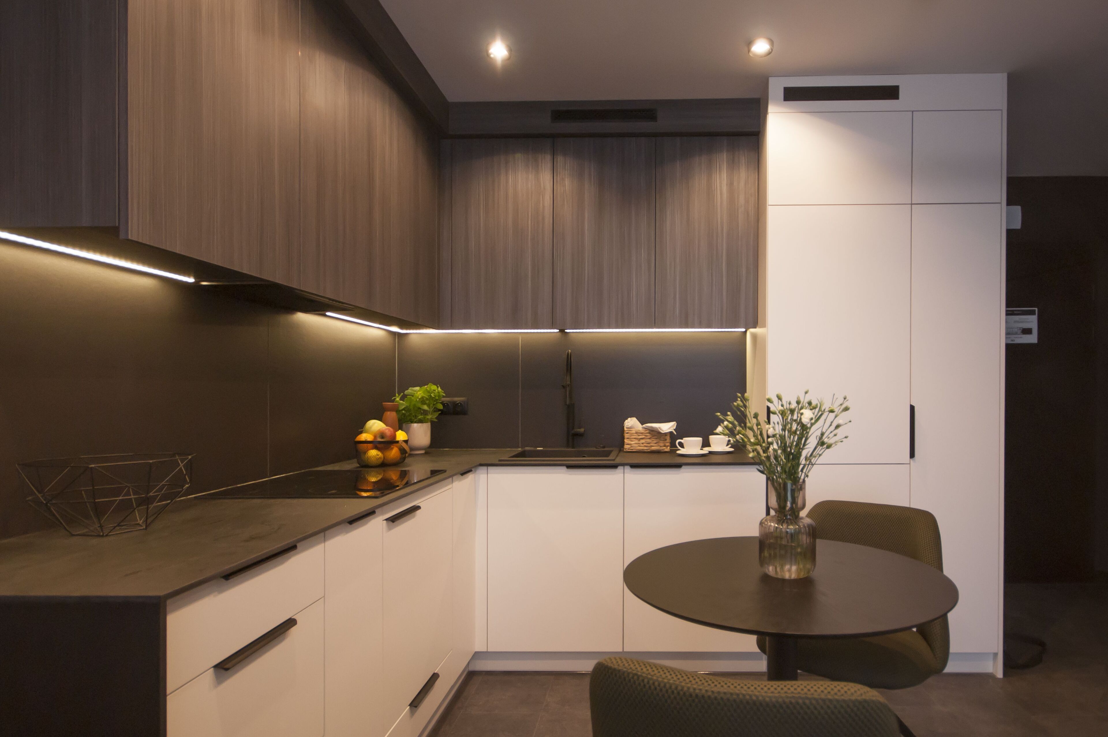A modern kitchen with a dark countertop, white cabinets, and a round dining table with chairs.