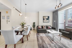En moderne stue med spiseplads, grå sofaer, et sofabord og et stort vindue med gardiner.