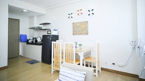 Eine kleine Küche mit Kühlschrank, Herd und Mikrowelle. Es gibt einen Esstisch mit Stühlen sowie eine kleine Couch. An der Wand hängt eine Karte.