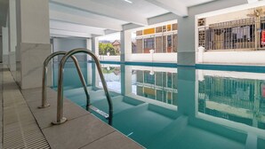 An indoor swimming pool with clear water, metal handrails, and a view of the outside through large windows.