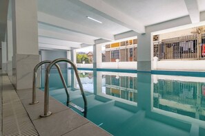 Una piscina interior con agua cristalina, barandales de metal y vistas al exterior a través de amplias ventanas.