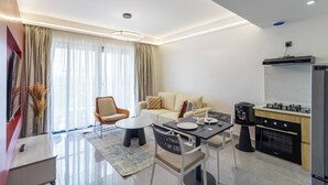 A modern living room with a sofa, armchair, dining table, and kitchen area with appliances.