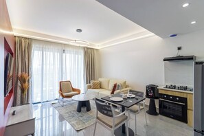 Una sala de estar moderna con sofá, sillón, mesa de comedor y zona de cocina con electrodomésticos.