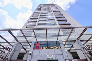 Un edificio alto con fachada de vidrio, un cartel que dice 'JAL RIA ONE' y un letrero de seguridad debajo.