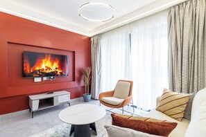 Een moderne woonkamer met een flatscreen televisie aan een rode muur, een ronde salontafel, een beige fauteuil en een bank met gestreepte kussens.