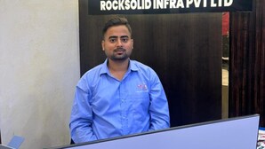 Un hombre de pie frente a un cartel de ARS ROCKSOLID INFRA PVT LTD.
