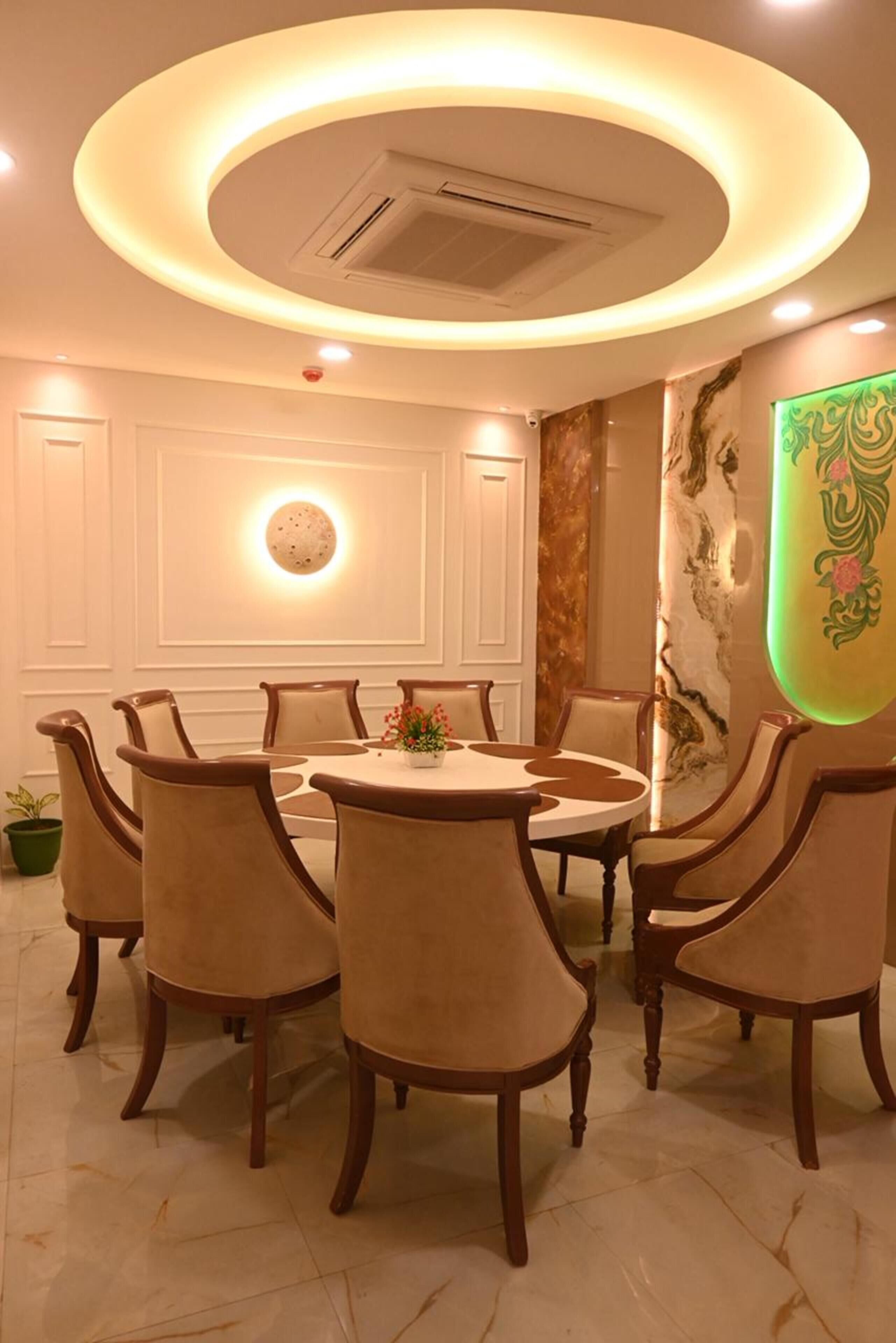 A dining area with a round table and six chairs, a ceiling light fixture, and a wall with a decorative panel.
