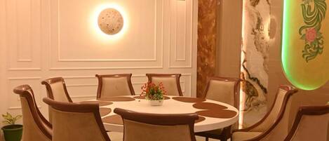 A dining area with a round table and six chairs, a ceiling light fixture, and a wall with a decorative panel.