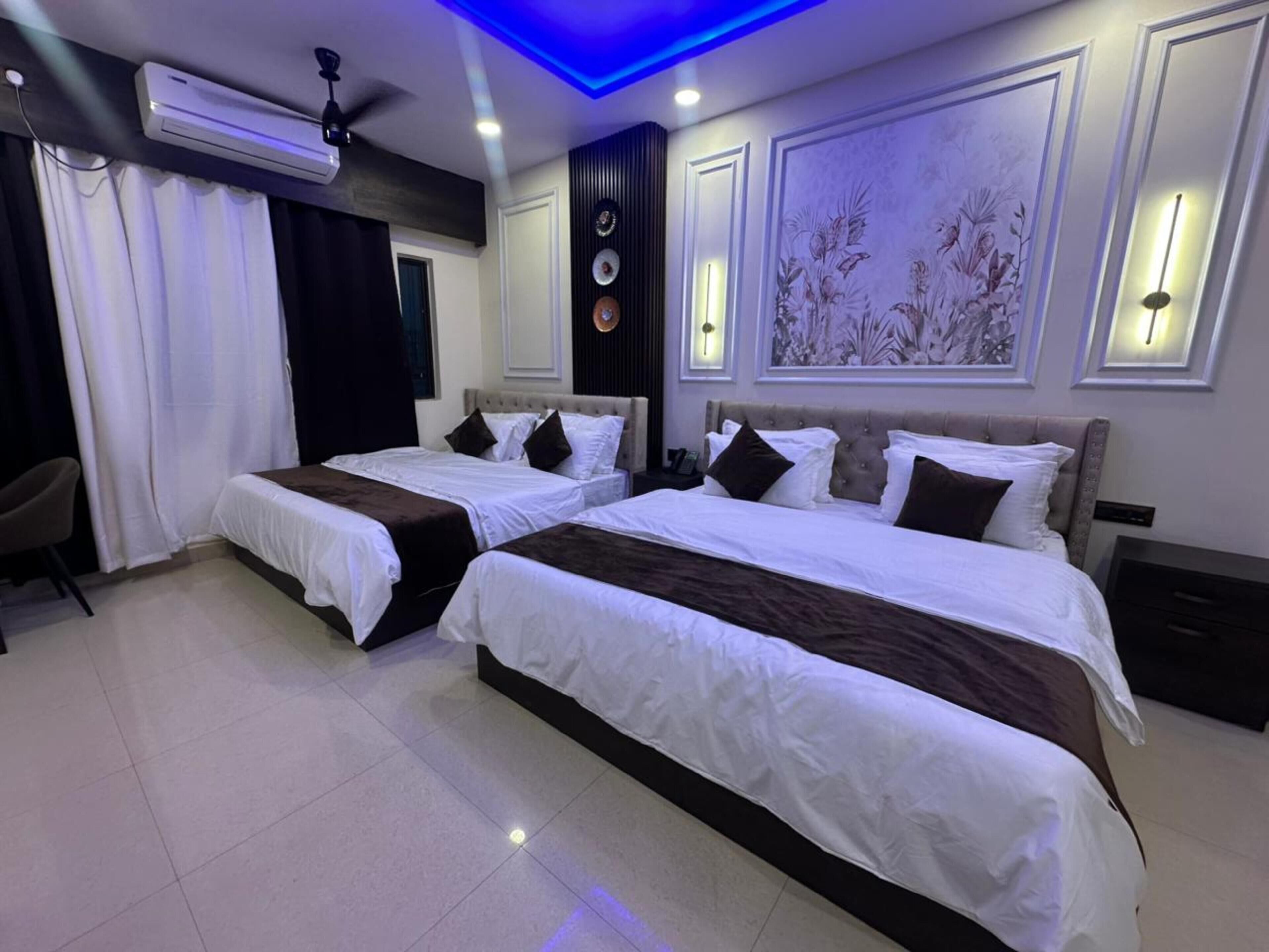 A hotel room with two beds, a ceiling fan, recessed lighting, a wall-mounted air conditioner, and a large floral painting.